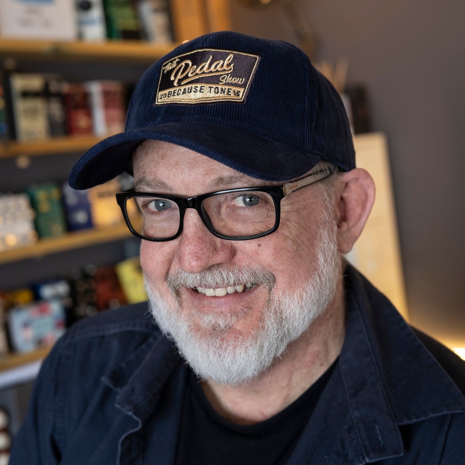Dan wears navy blue cord baseball cap with vintage That Pedal Show logo embroidered onto front.