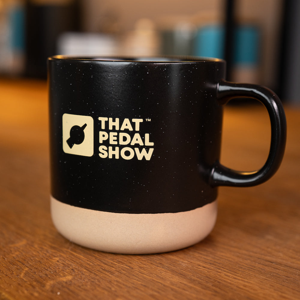 Ceramic black dipped glaze mug with a speckled finish and That Pedal Show logo printed on the side.