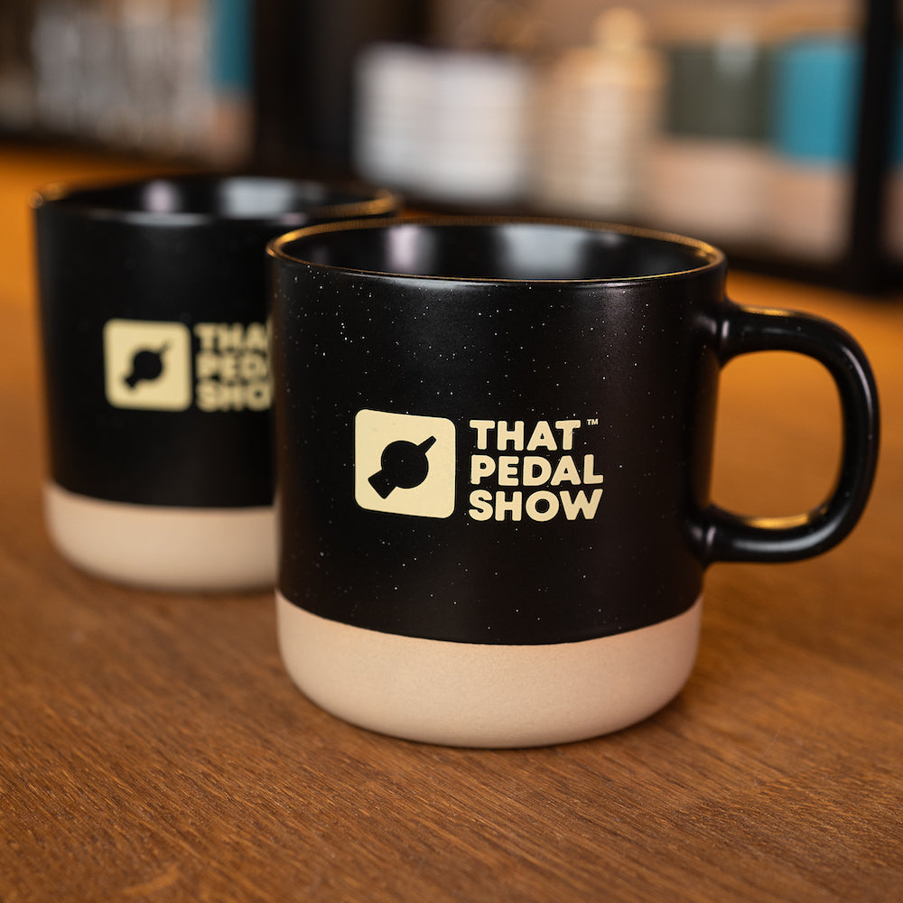 A pair of black ceramic dipped glaze mugs with a speckled finish and That Pedal Show logo printed on the side.