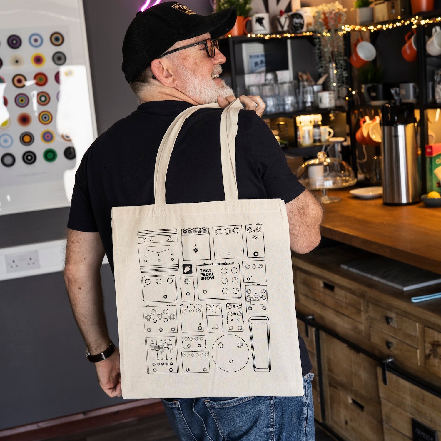 Dan from That Pedal Show models a cream cotton tote bag with a black line art graphic of vintage guitar pedals. 