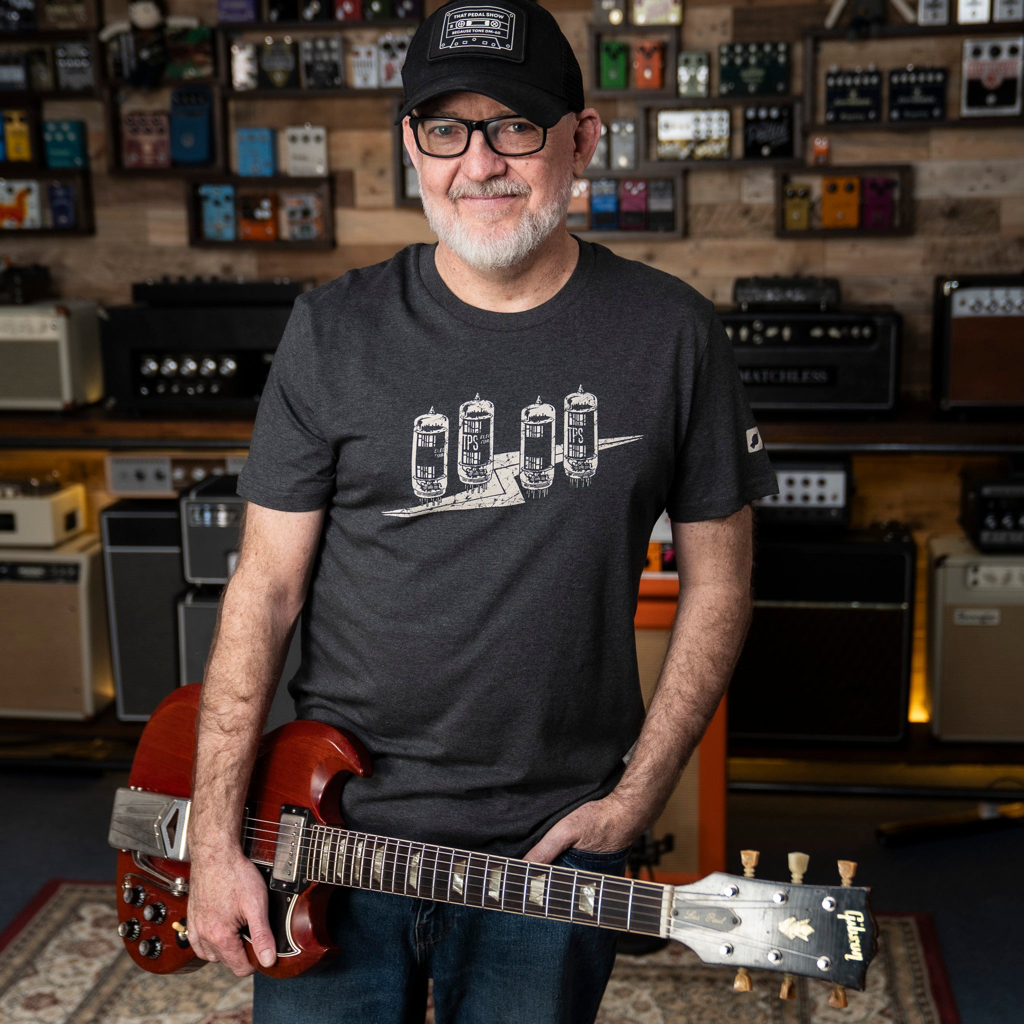Dan wearing a 'Tubeflash' t-shirt from That Pedal Show holding a red Gibson guitar in the TPS Studio.