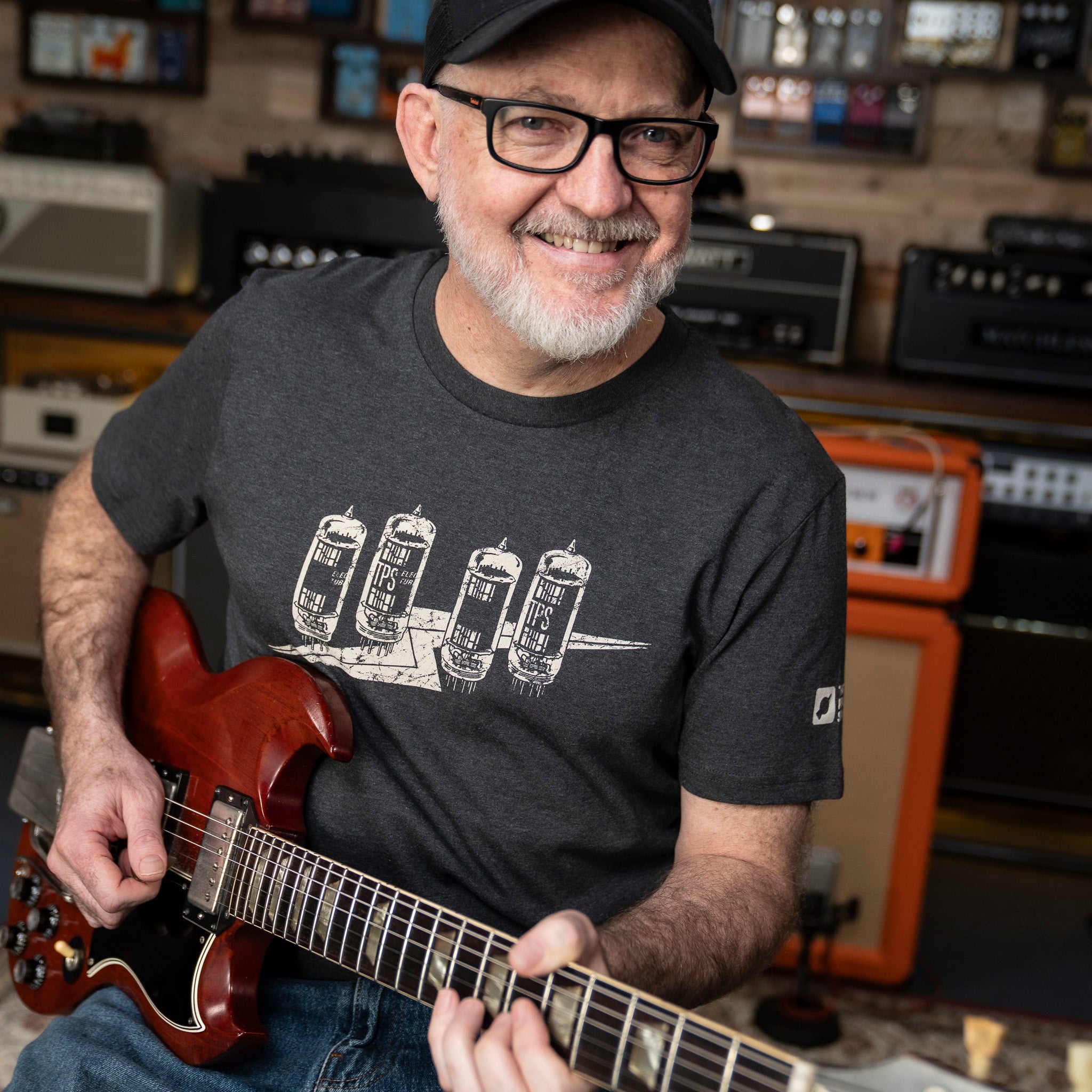 Dan wearing a 'Tubeflash' t-shirt from That Pedal Show holding a Gibson guitar in the TPS Studio.
