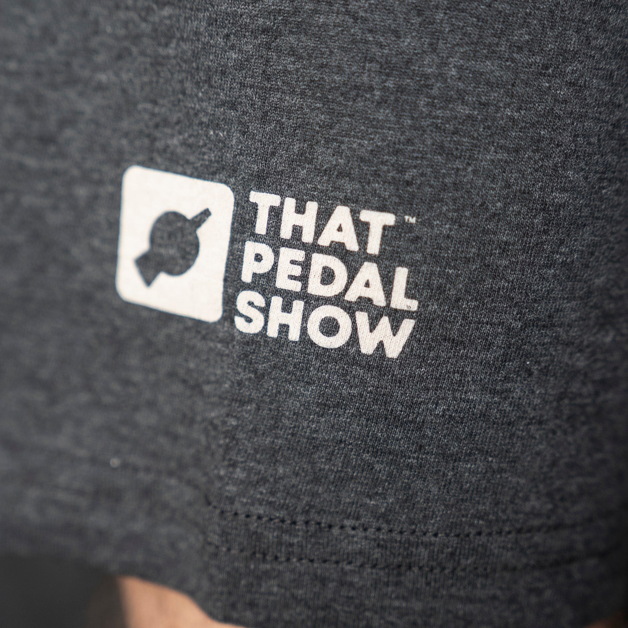 Close up of That Pedal Show logo on the sleeve of a grey t-shirt