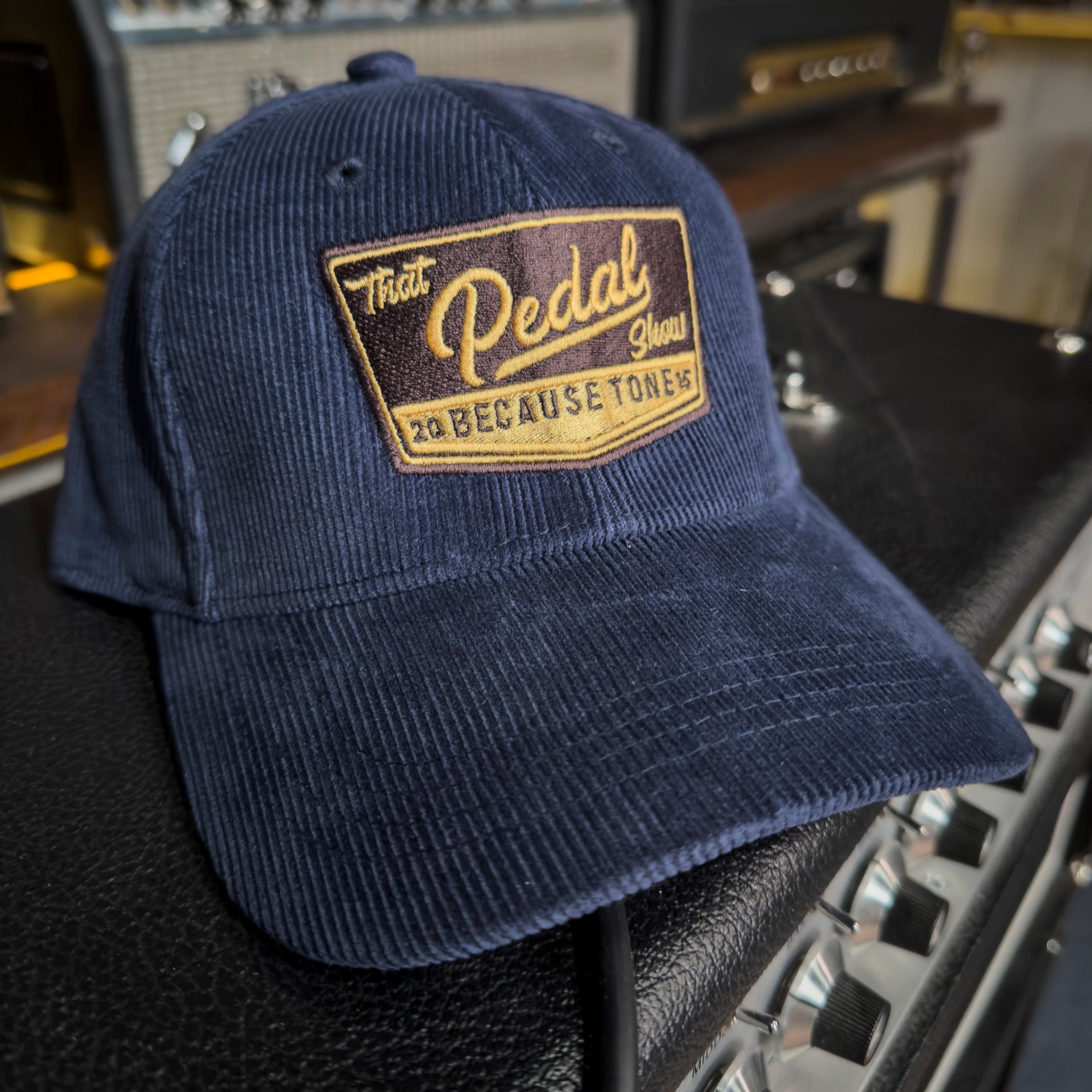 Navy cord baseball cap with vintage That Pedal Show logo embroidered onto front resting on top of a guitar amp.