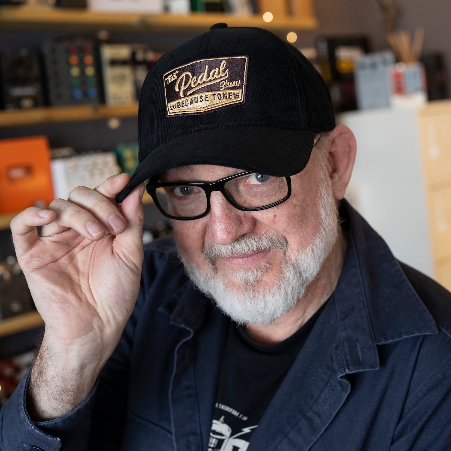 Dan wears black cord baseball cap with vintage That Pedal Show logo embroidered onto front.